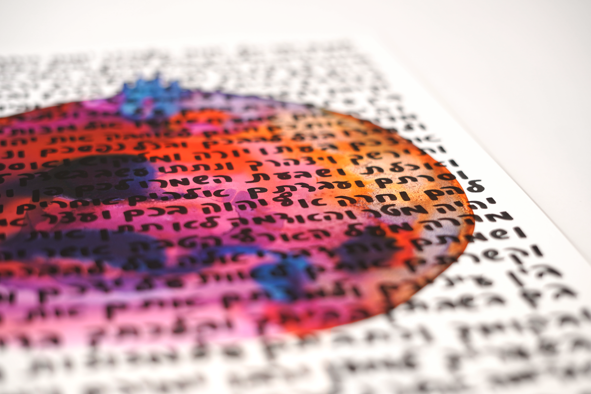 Close-up of the liquid watercolor pomegranate and handwritten Hebrew lettering on museum-grade paperboard
